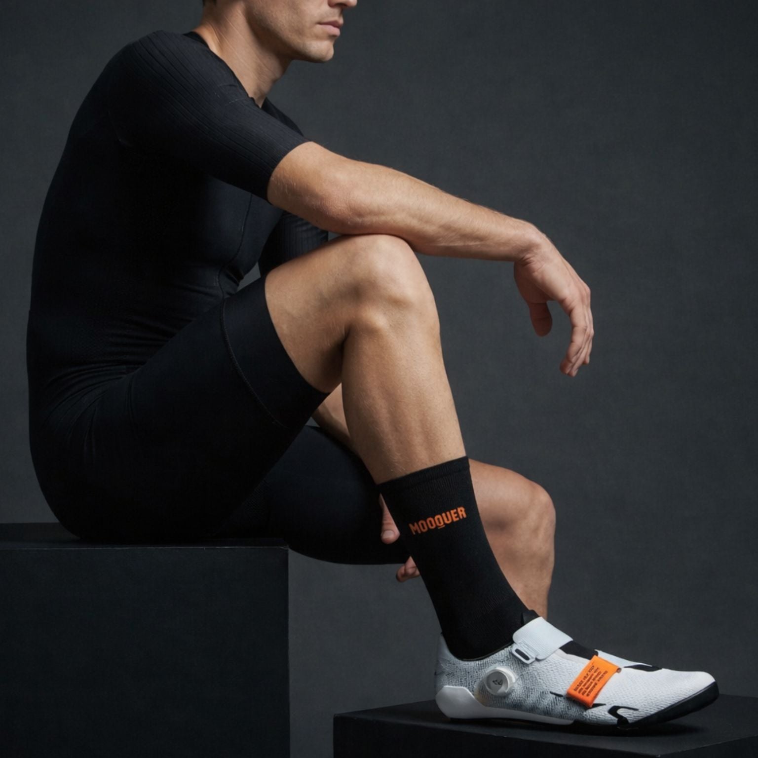 ciclista sentado con calcetines Mooquer barefoot negros y zapatillas ciclismo S-Works en fondo oscuro