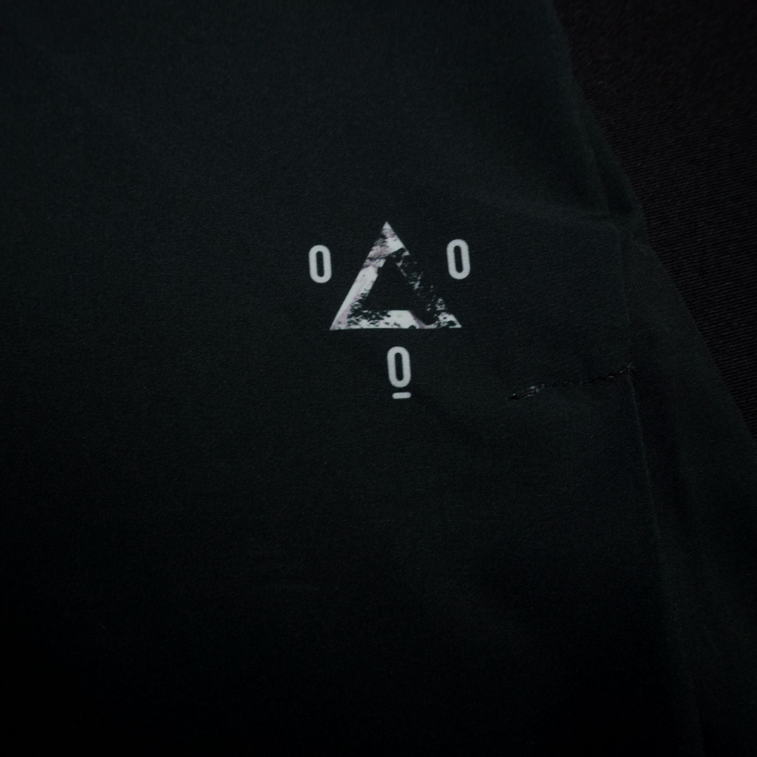 Logo triangular Mooquer serigrafiado en gris oscuro sobre tejido negro del pantalón running