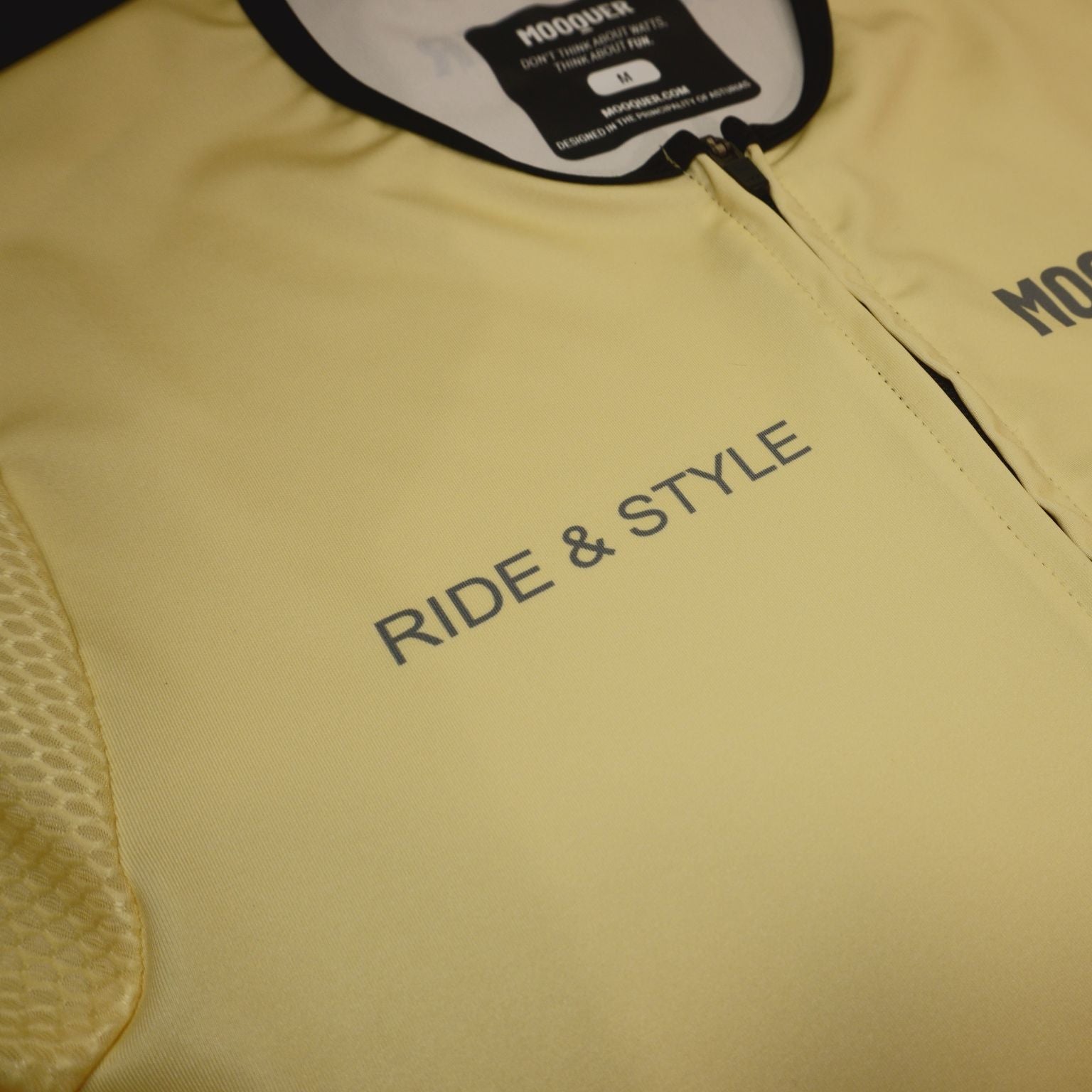 Maillot ciclismo crema Mooquer con cremallera frontal y tipografía corporativa en gris verdoso oscuro